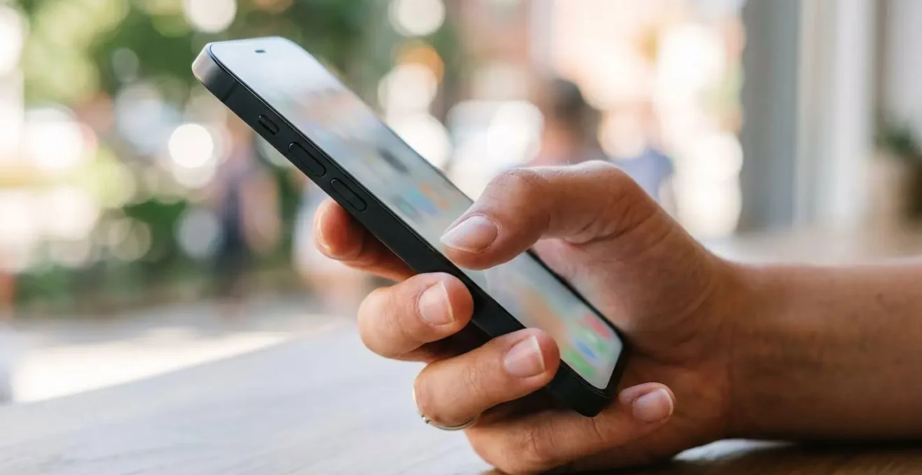 Eine Hand hält ein Smartphone mit vollständig unscharfem Bildschirm vor einem verschwommenen modernen Arbeitsumfeld